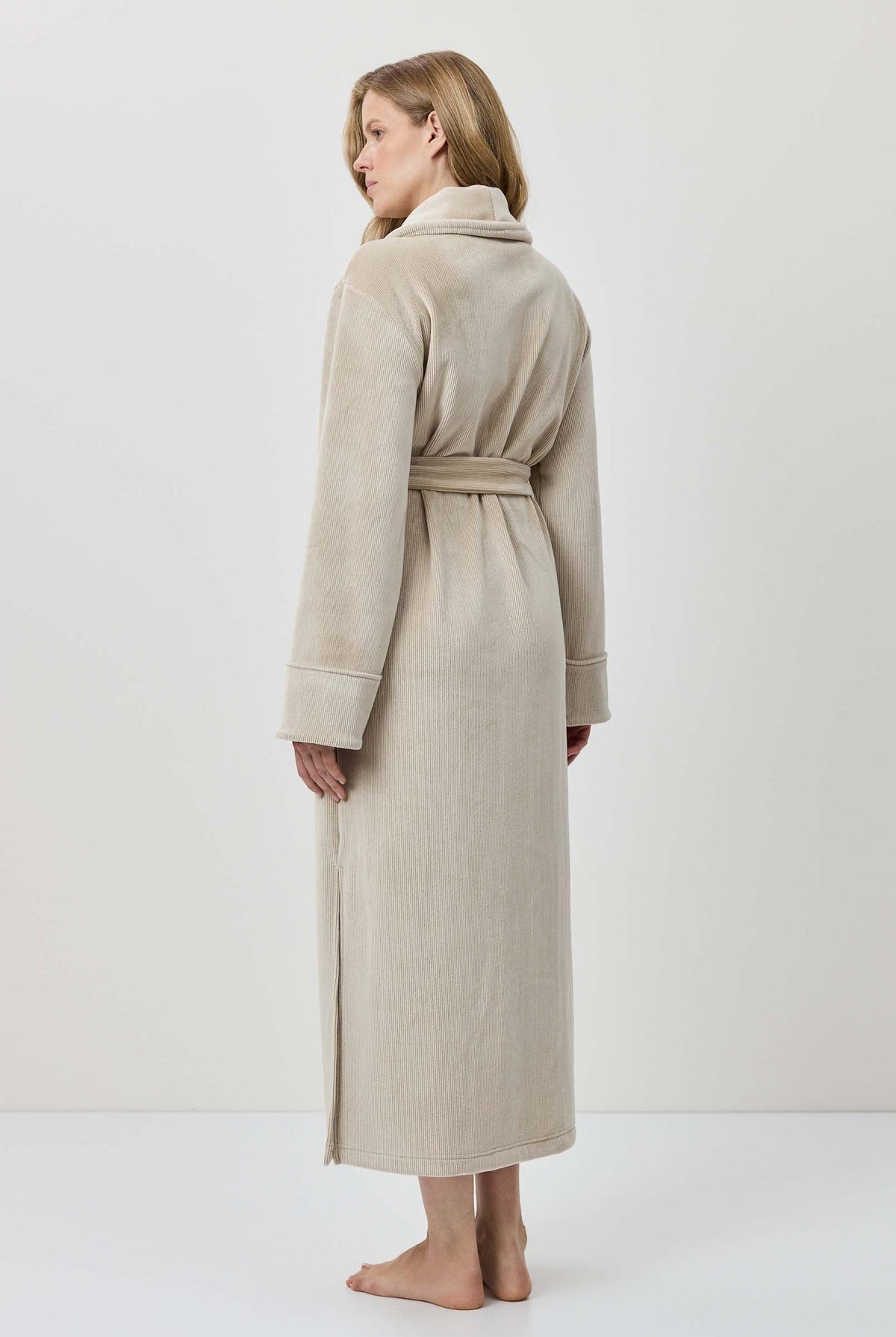Woman wearing a beige robe standing against a white background