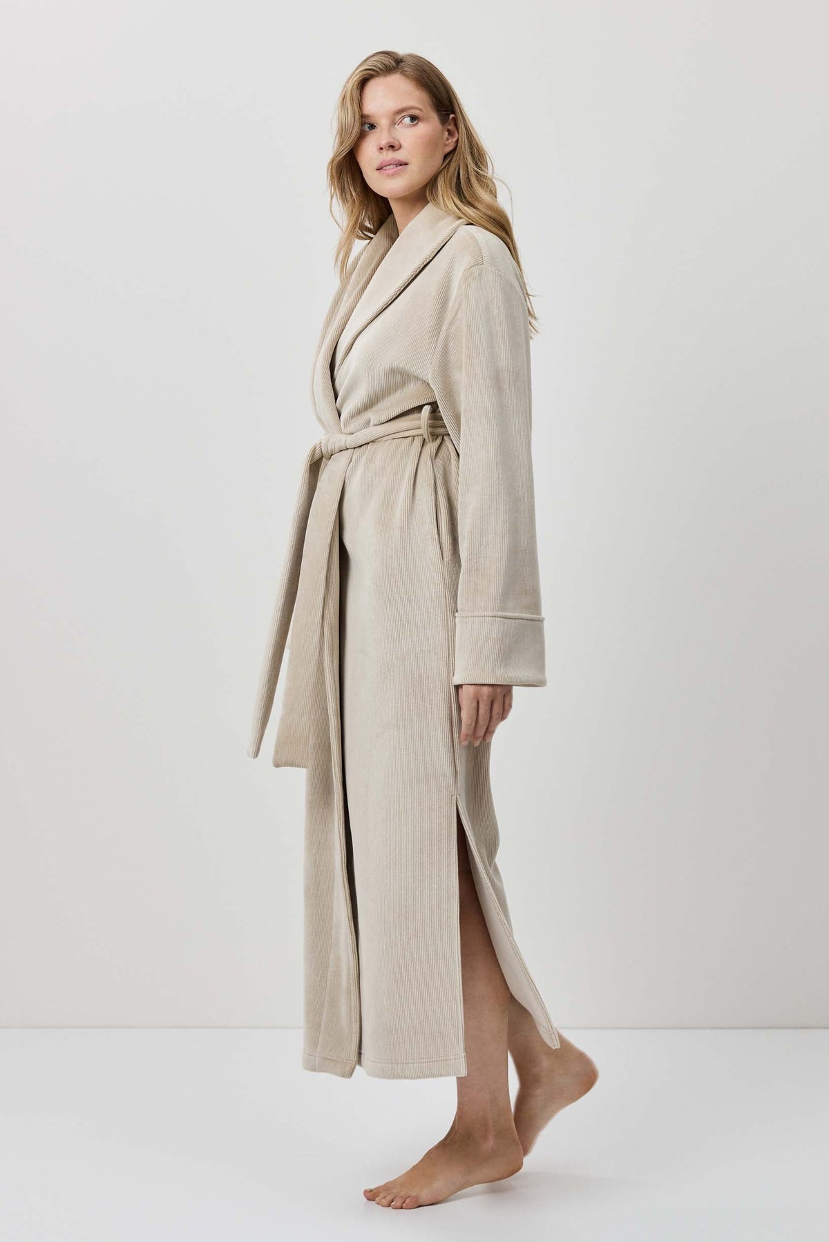 Woman wearing a beige robe standing against a white background