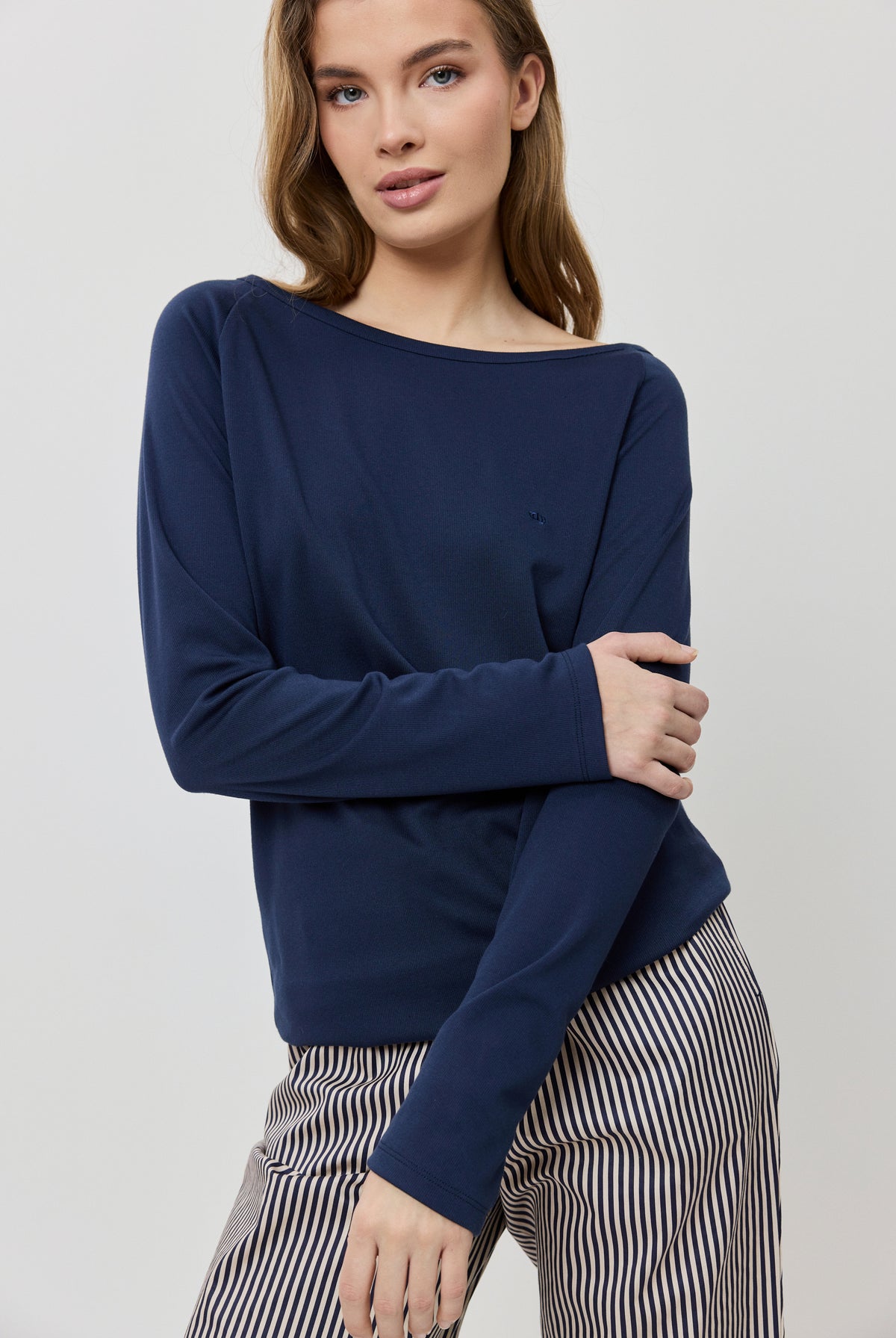 Woman wearing a navy blue sweater and striped pants on a light gray background