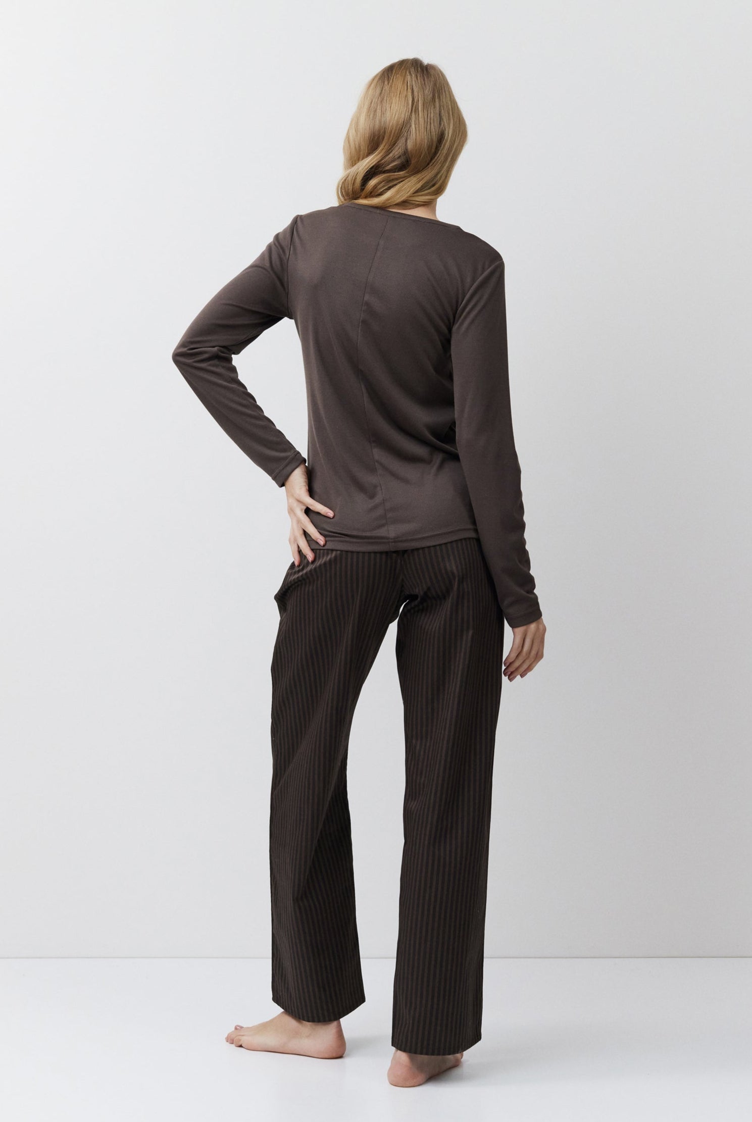 Person wearing a brown long-sleeve top and pants on a white background