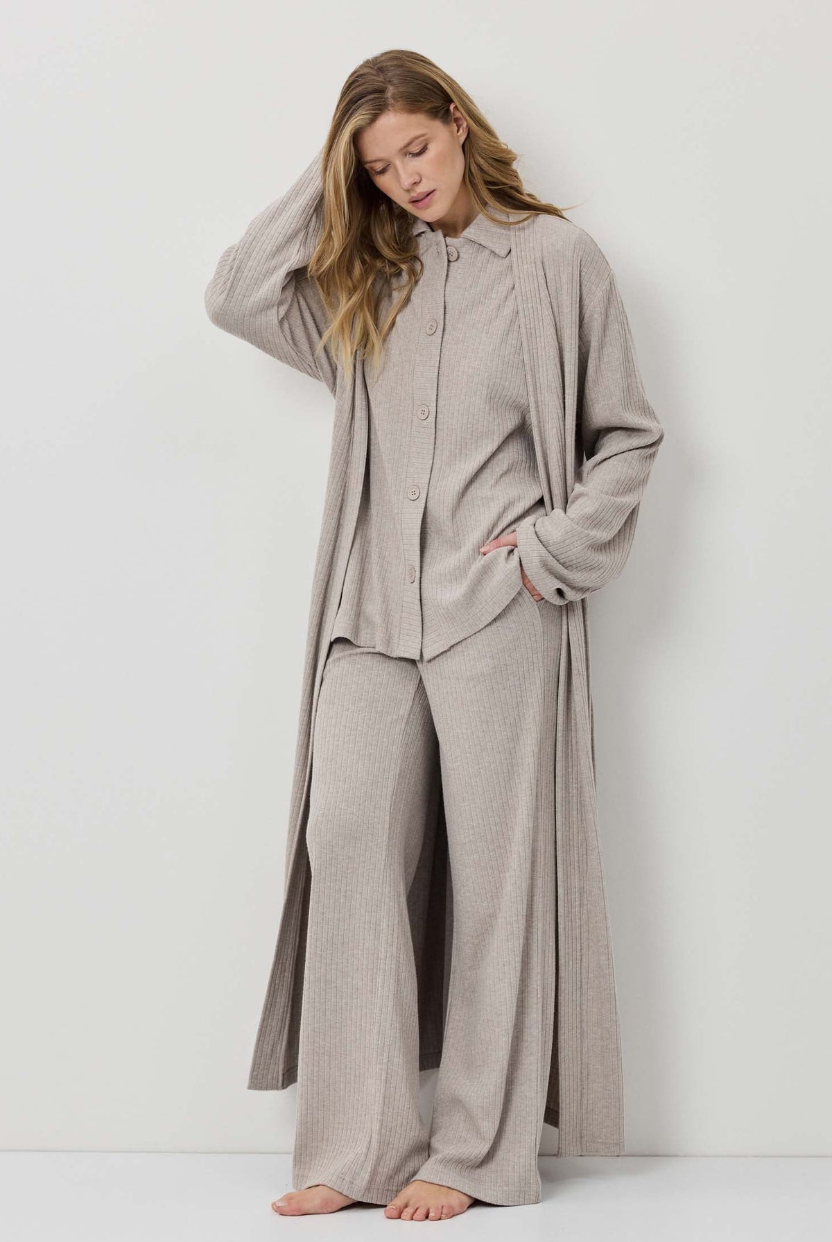 Woman wearing a beige long-sleeve shirt and wide-leg pants against a white background