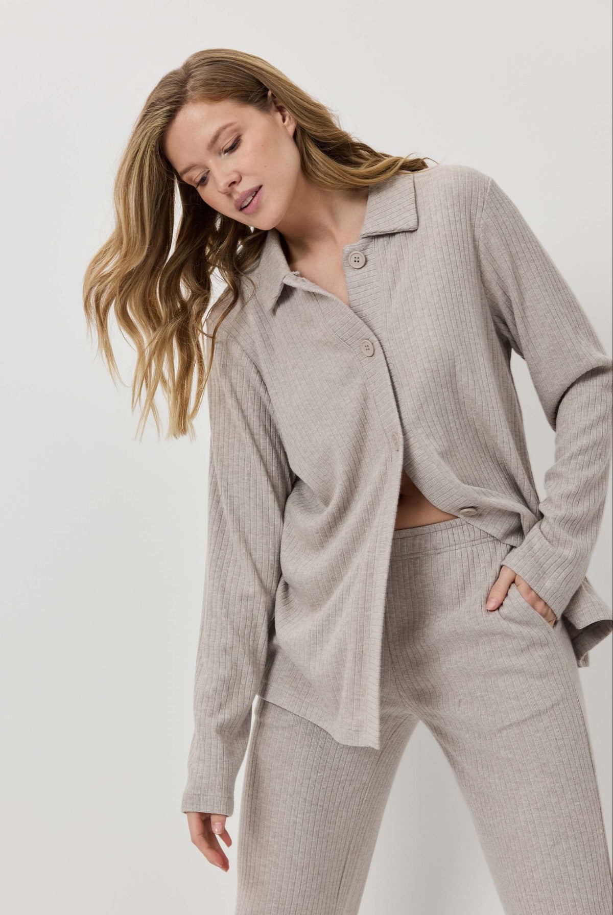 Woman wearing a beige ribbed pajama set against a white background