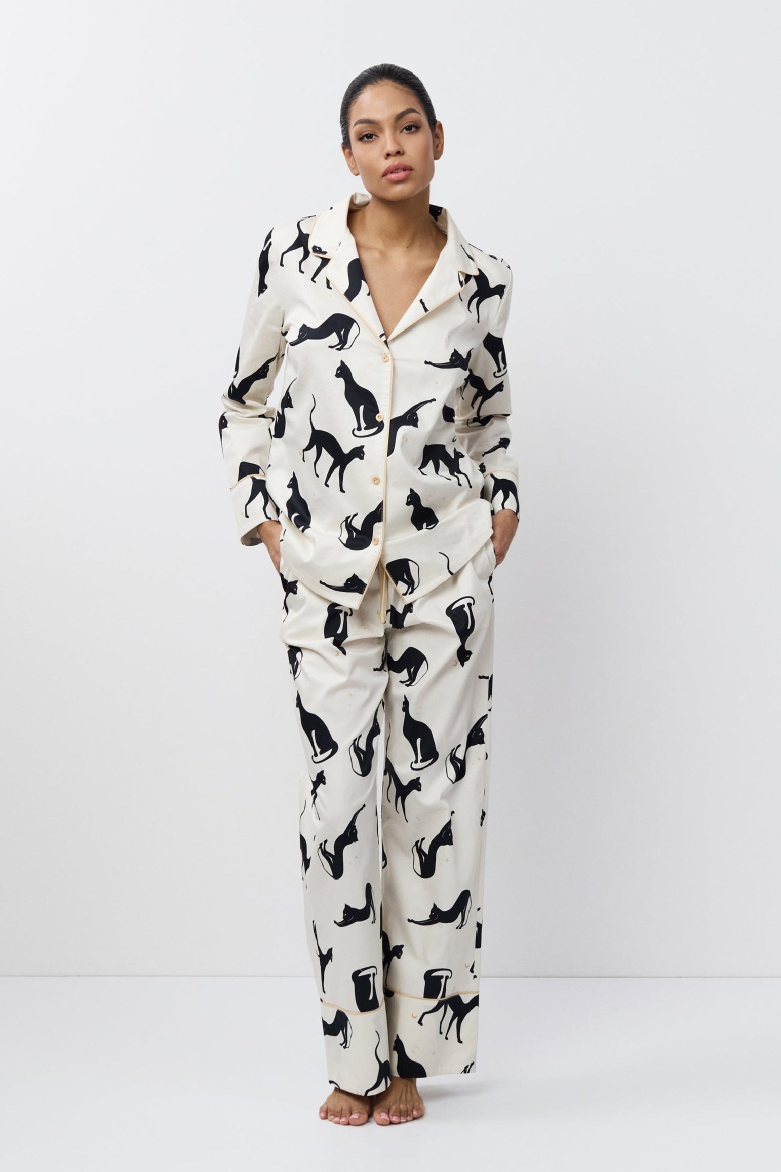 Person wearing a white pajama set with black cat prints on a white background
