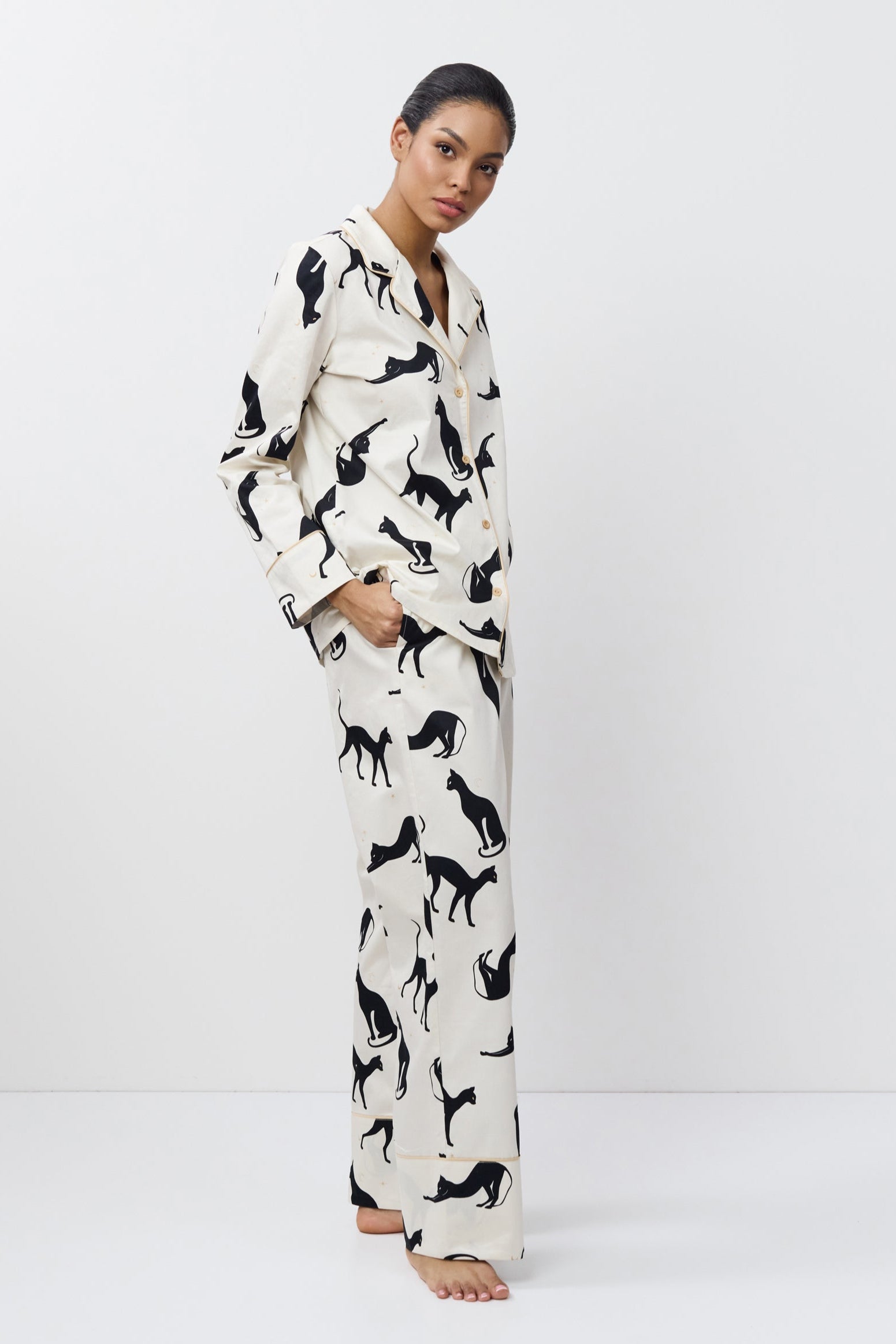 Woman wearing a pajama set with black cat prints on a white background