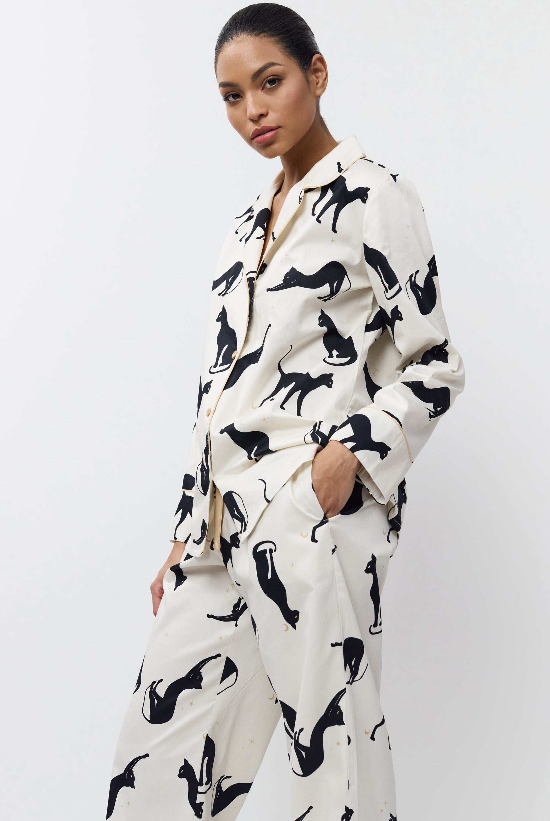 Woman wearing a white pajama set with black cat pattern on a white background