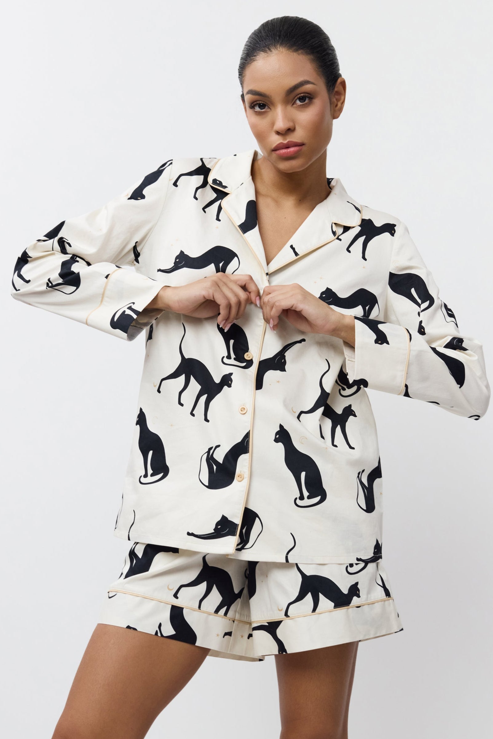 Woman wearing a pajama set with black cat prints on a white background
