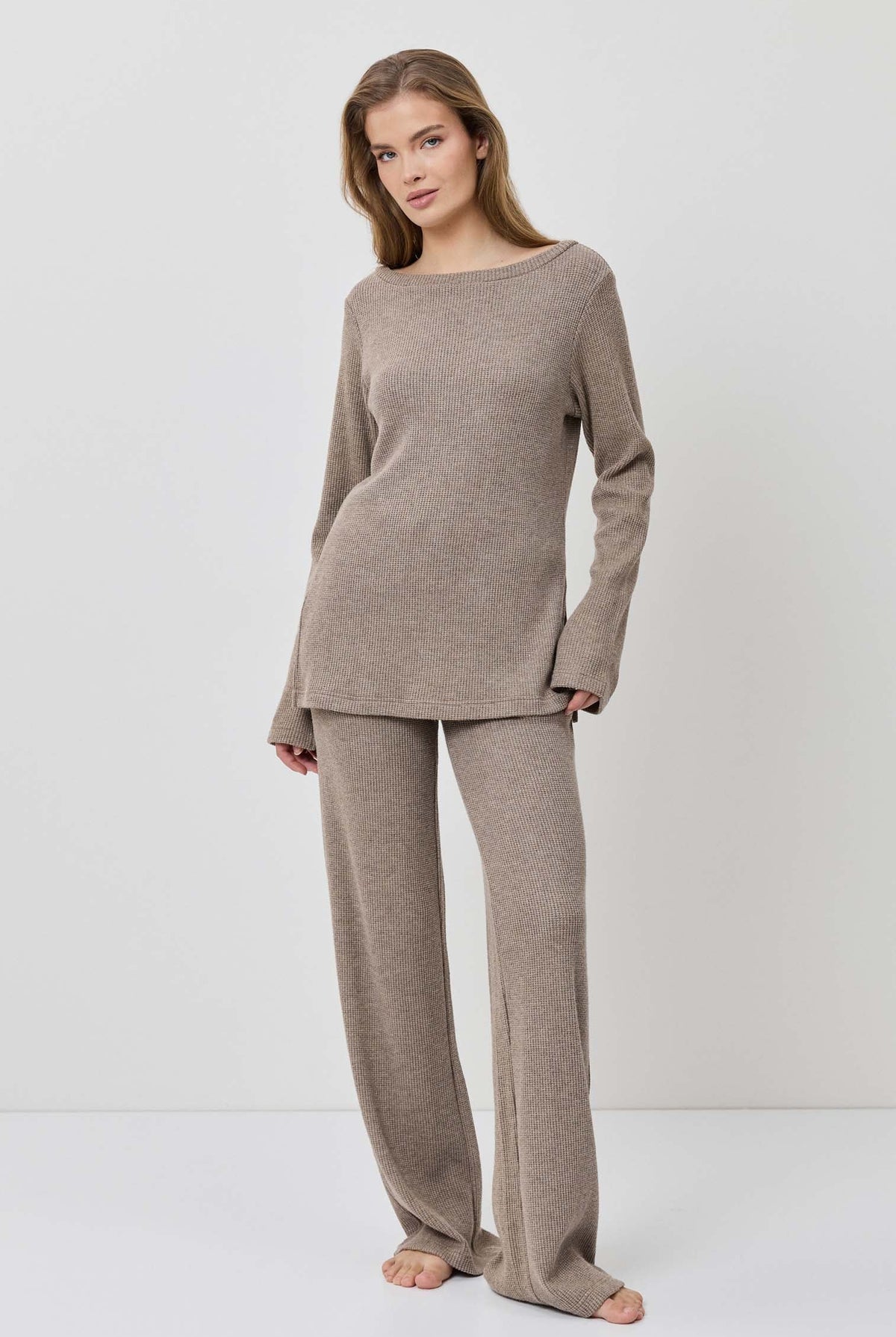 Woman wearing a beige long-sleeve top and pants on a white background