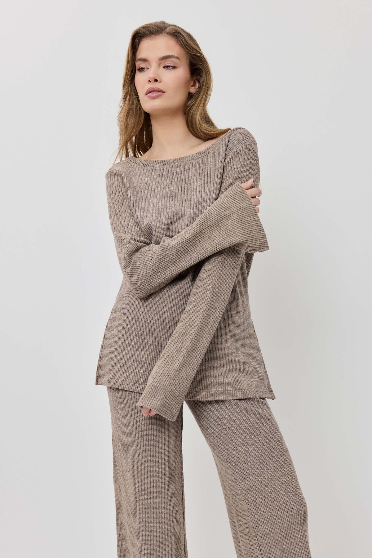 Woman wearing a beige sweater and pants on a light gray background