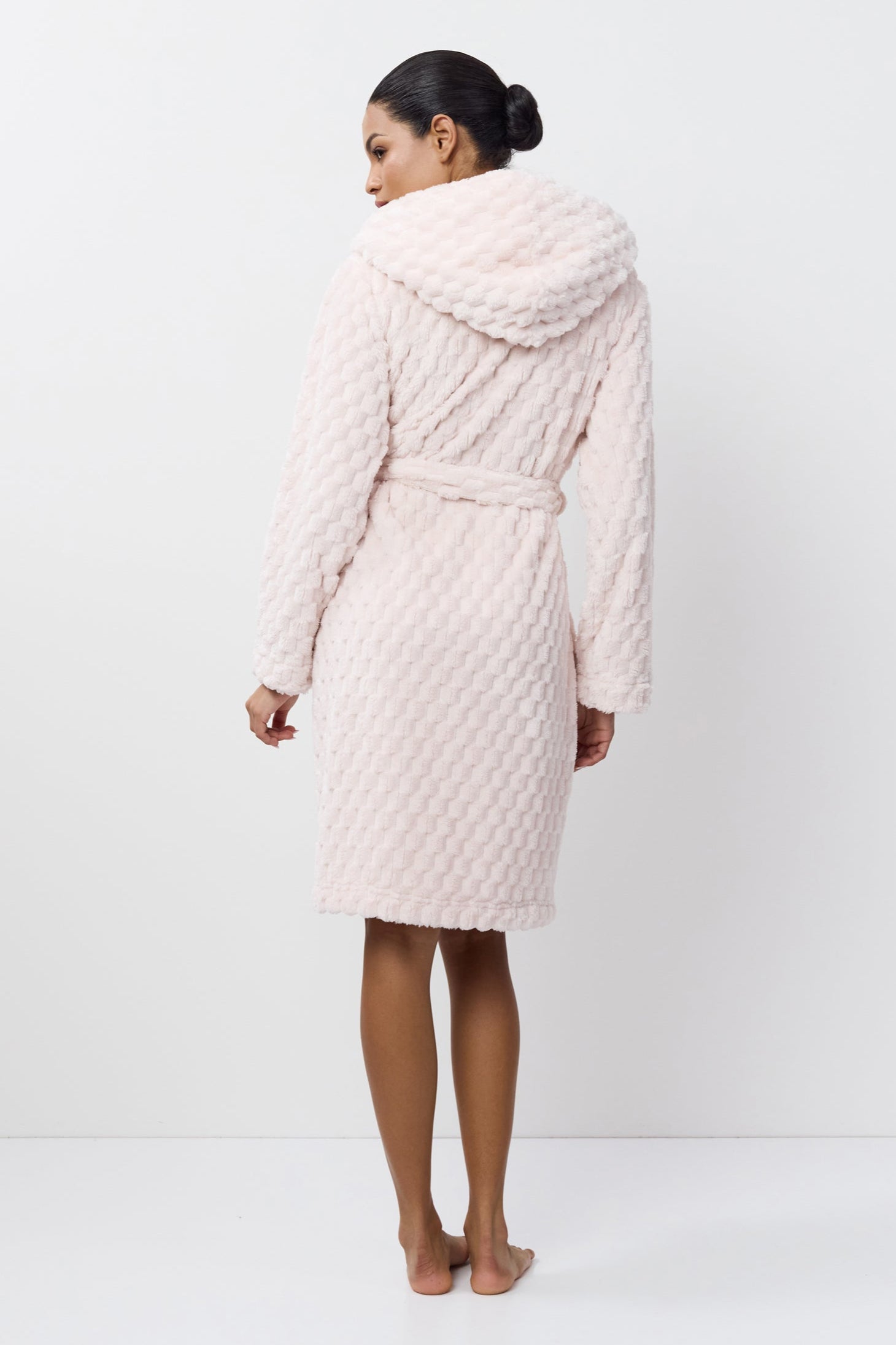 Person wearing a light pink quilted bathrobe on a white background