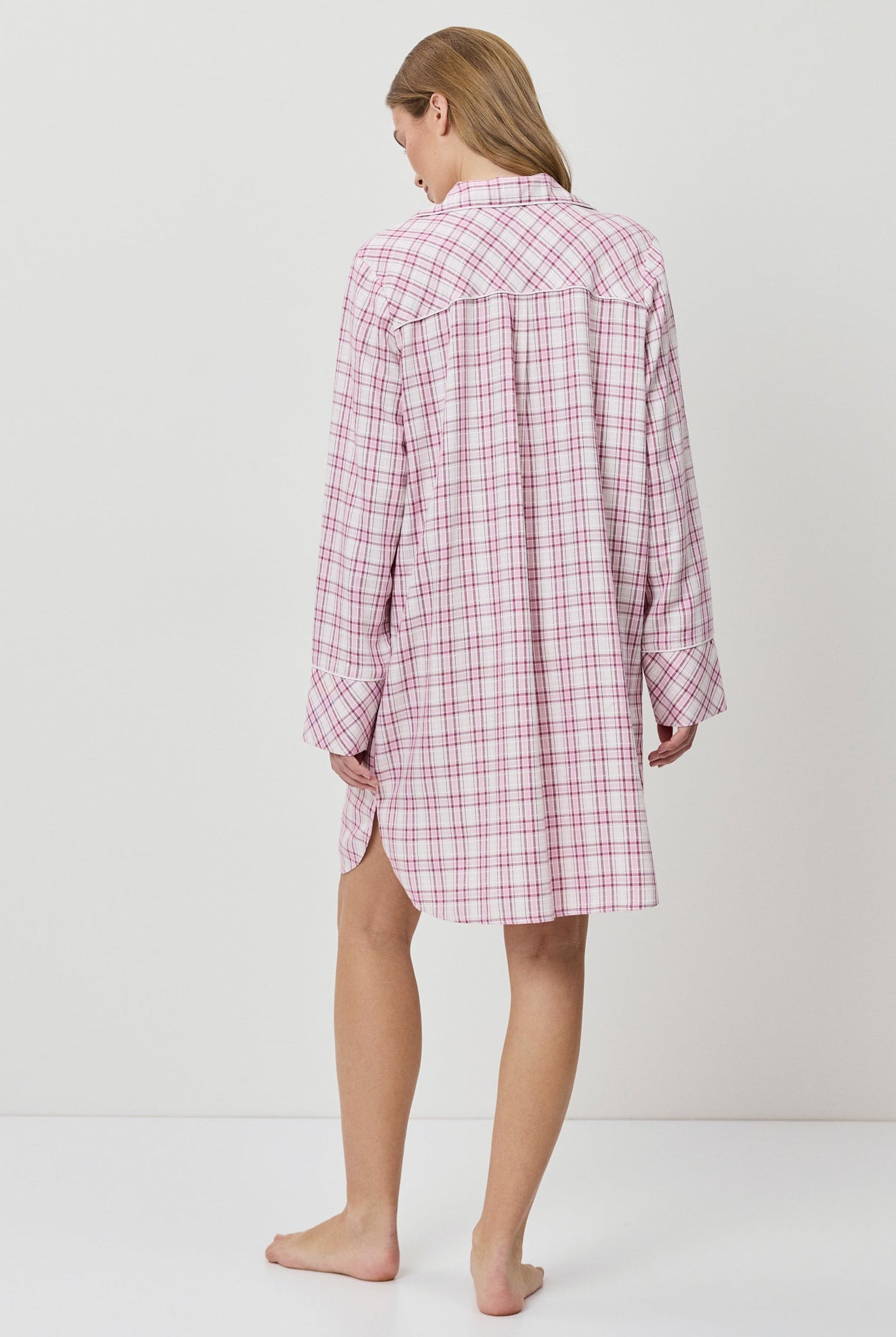 Person wearing a pink and white checkered nightshirt on a plain background