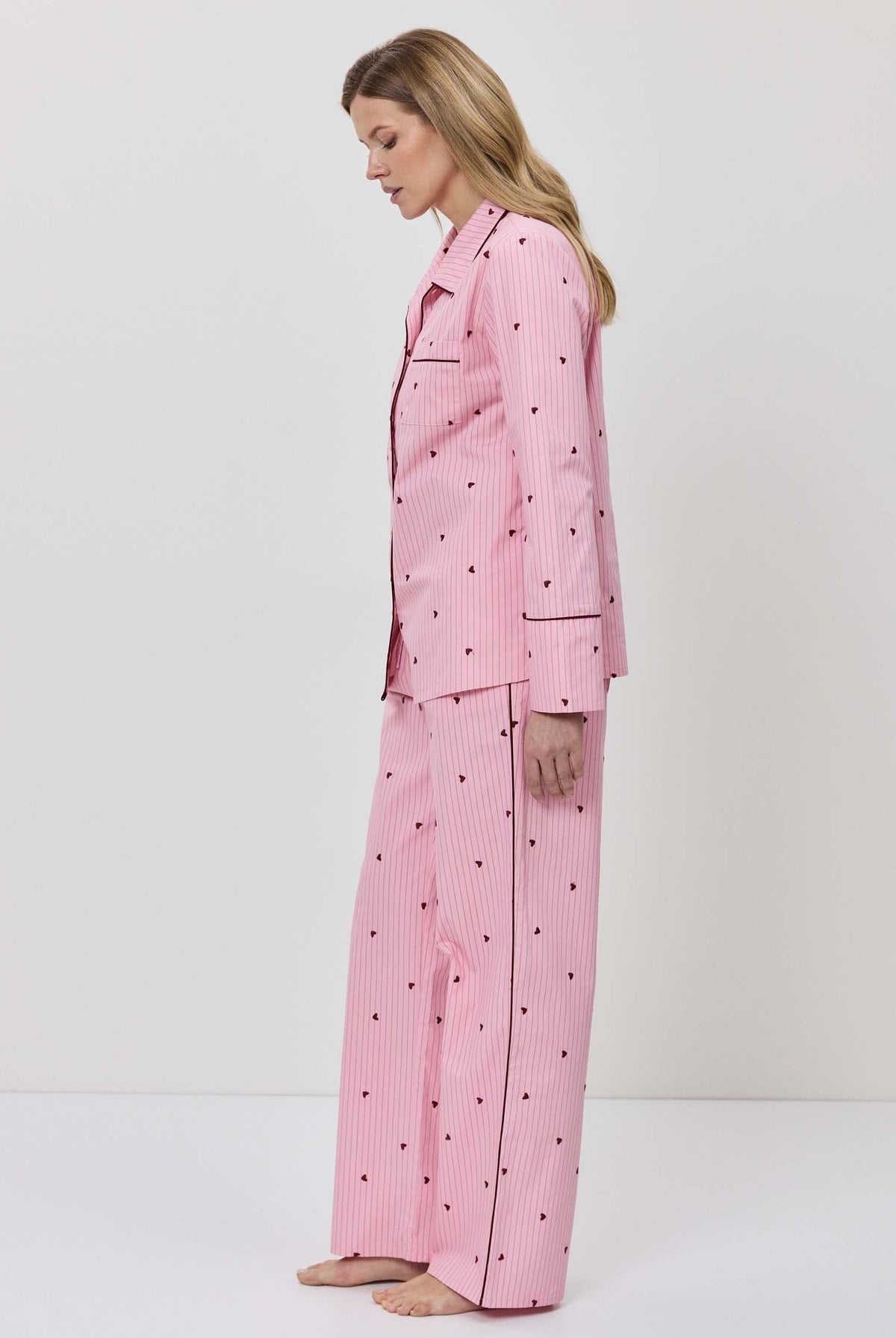 Person wearing a pink pajama set with hearts on a white background
