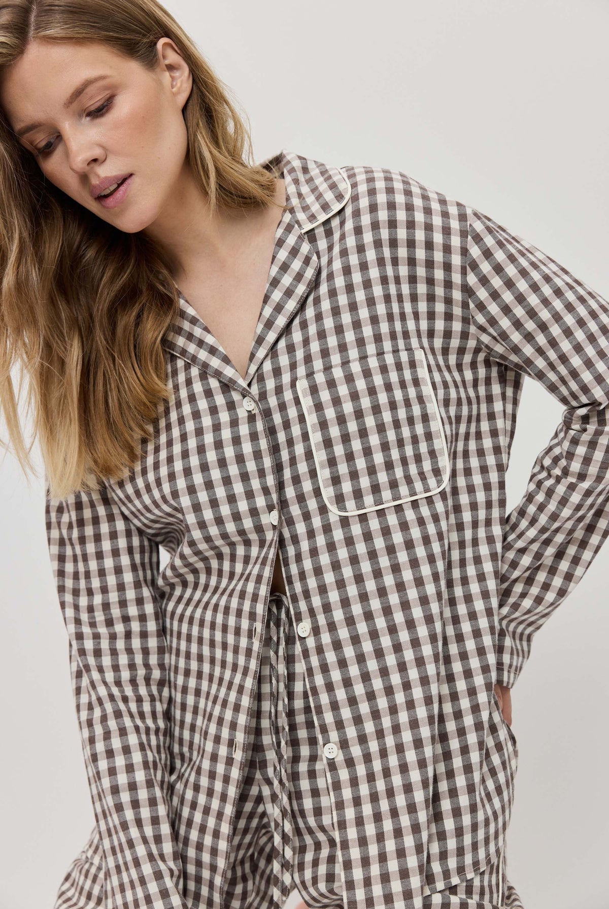 Woman wearing a brown and white checkered pajama set against a plain background
