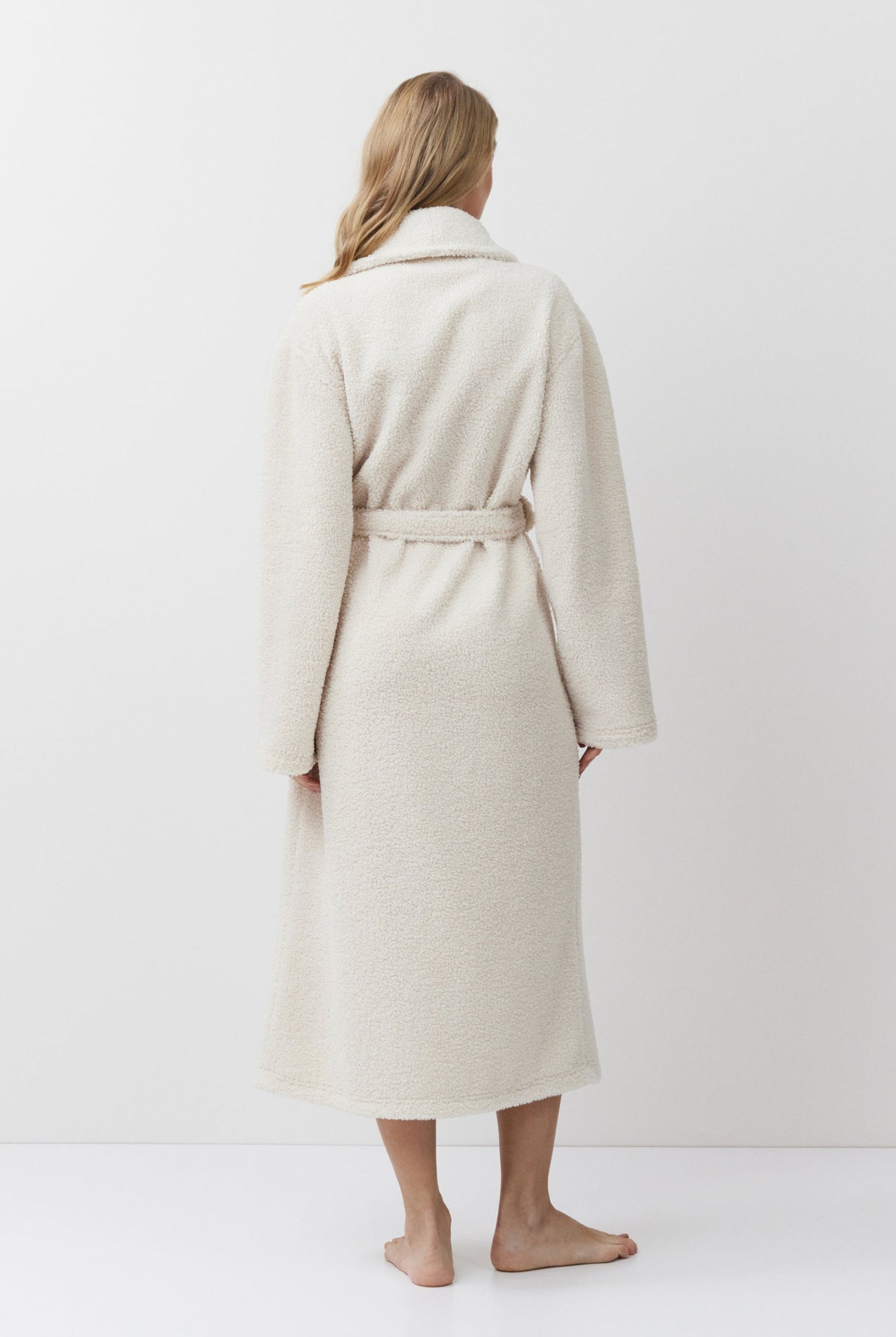 Person wearing a beige bathrobe standing against a white background