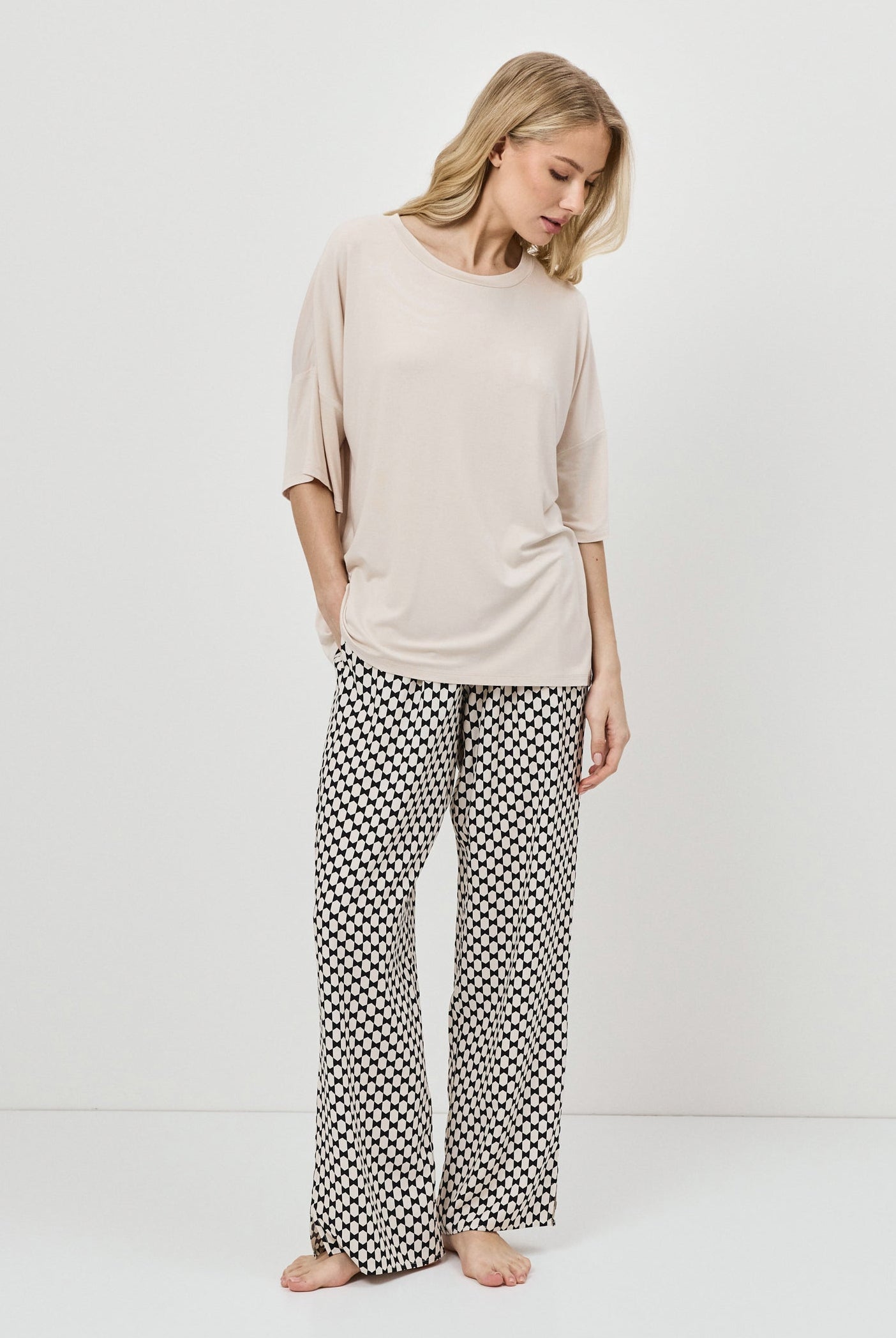 Woman wearing a beige top and patterned pants on a white background