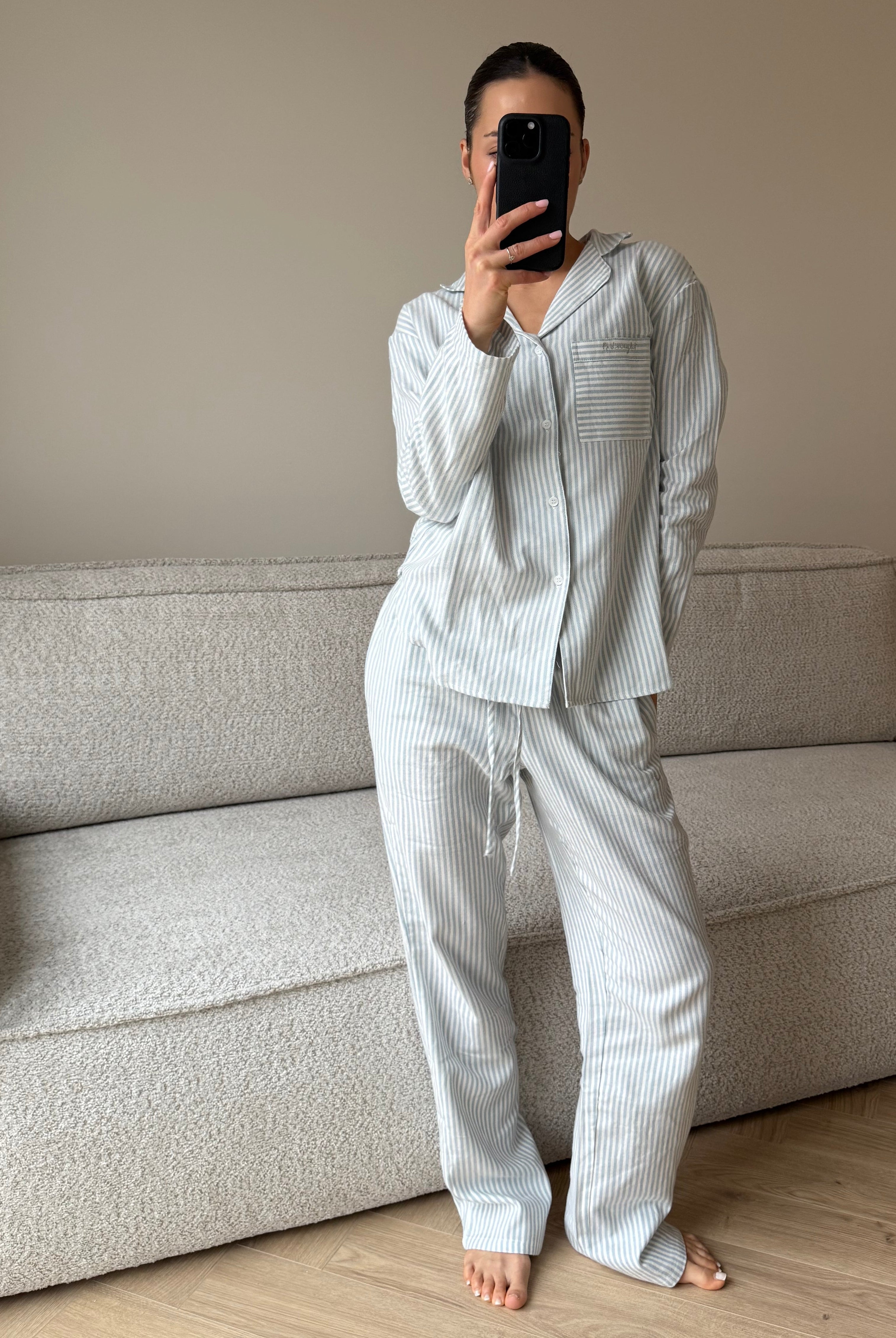 Person wearing a light-colored pajama set standing in a room with a sofa.