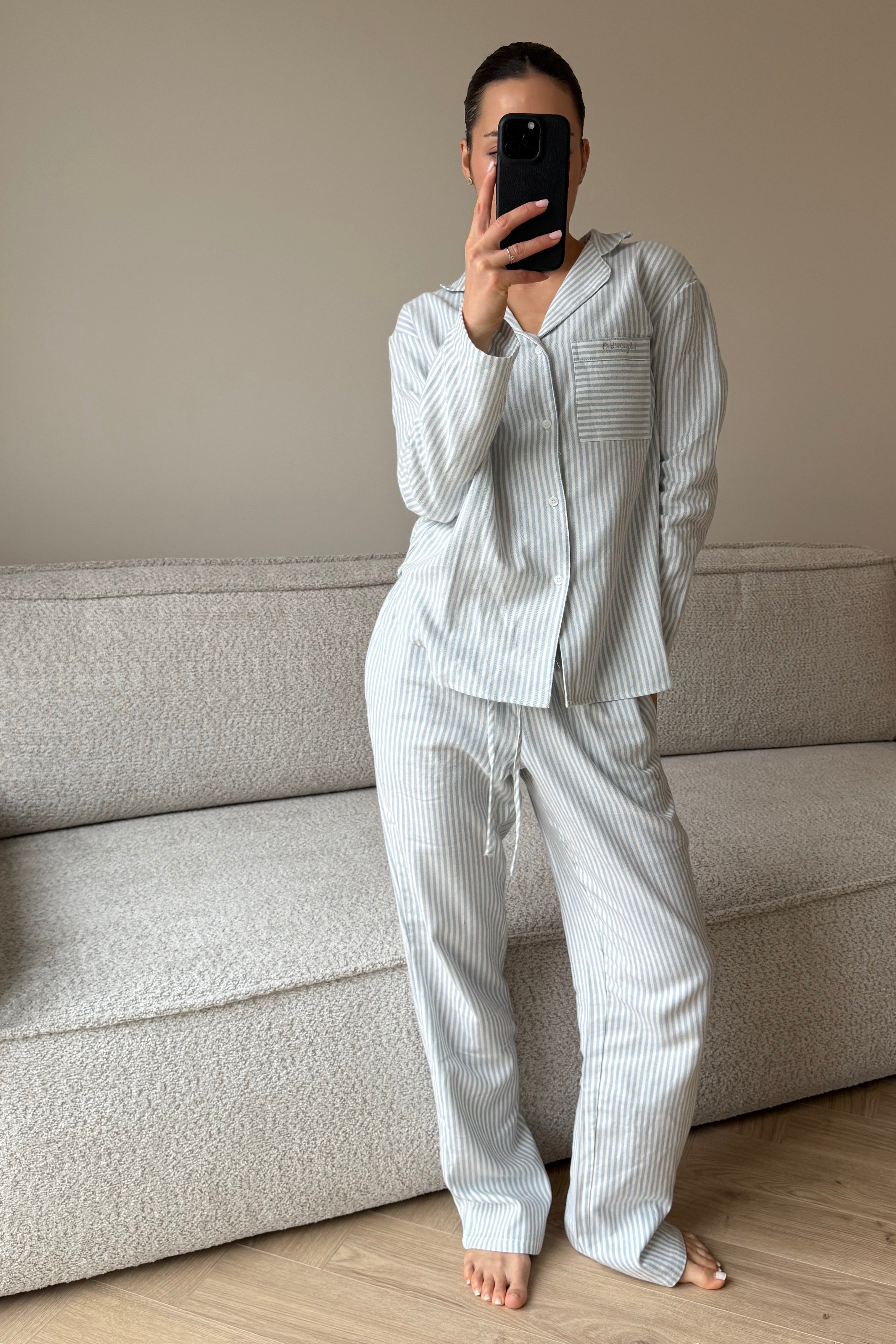 Person wearing a light-colored pajama set standing in a room with a sofa.