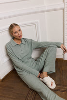 Woman in a green outfit sitting on a wooden floor against a white wall.