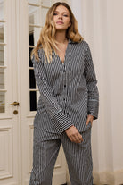 Woman wearing a black and white striped outfit standing in a room with white walls and a door.