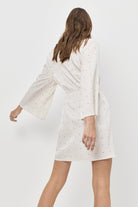 Woman wearing a white dress with bell sleeves on a plain background