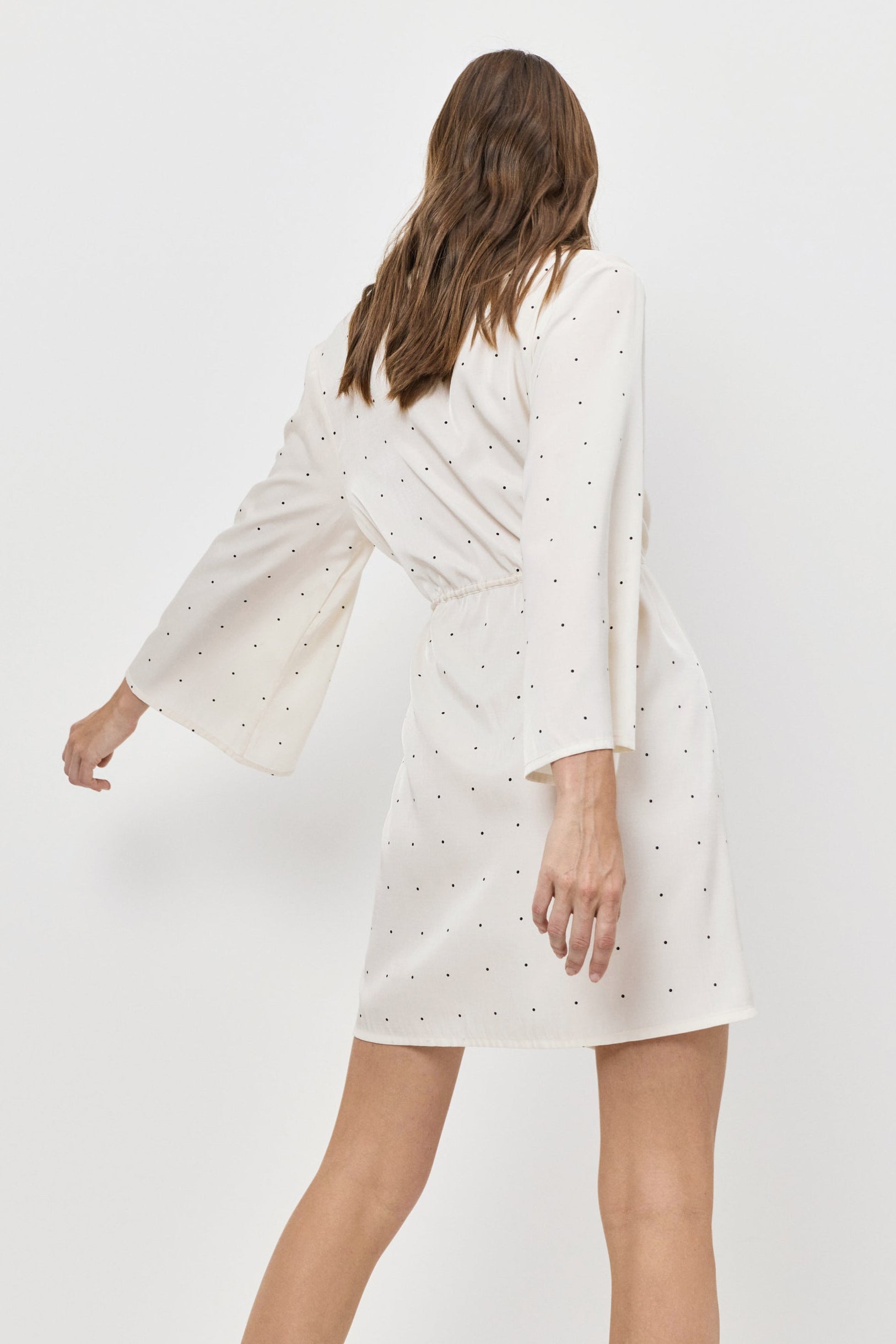 Woman wearing a white dress with bell sleeves on a plain background