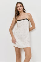 Woman wearing a white nightdress with black lace trim on a plain background