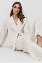 Woman wearing a white polka dot pajama set sitting on a bed against a white background