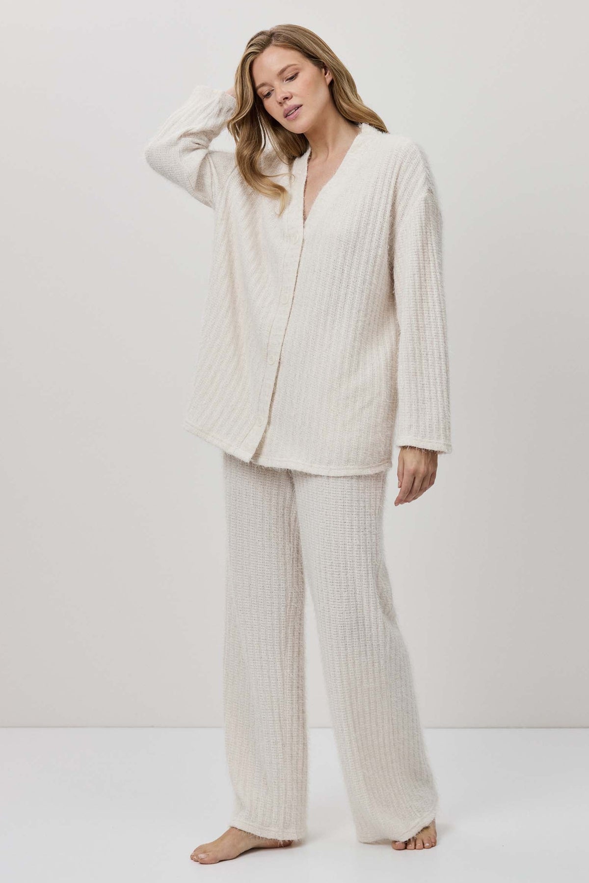 Woman wearing a white ribbed pajama set against a white background