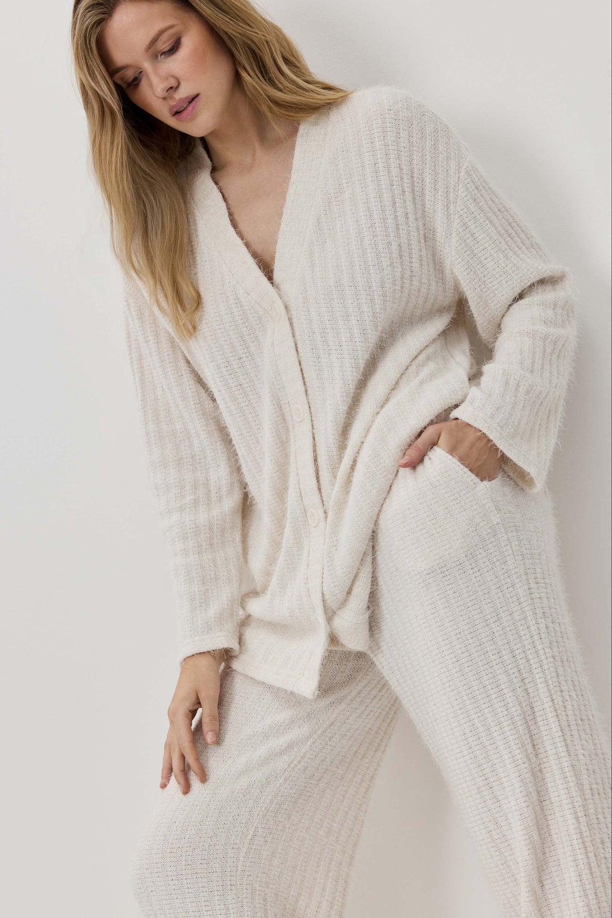 Woman wearing a cream-colored cardigan and pants against a white background