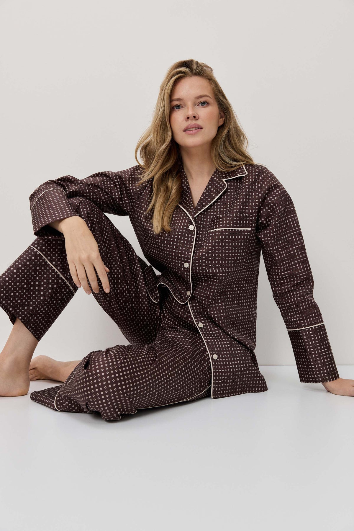 Woman wearing a brown polka dot pajama set sitting on a white surface.