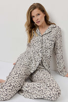 Woman wearing a leopard print pajama set sitting on a white surface.