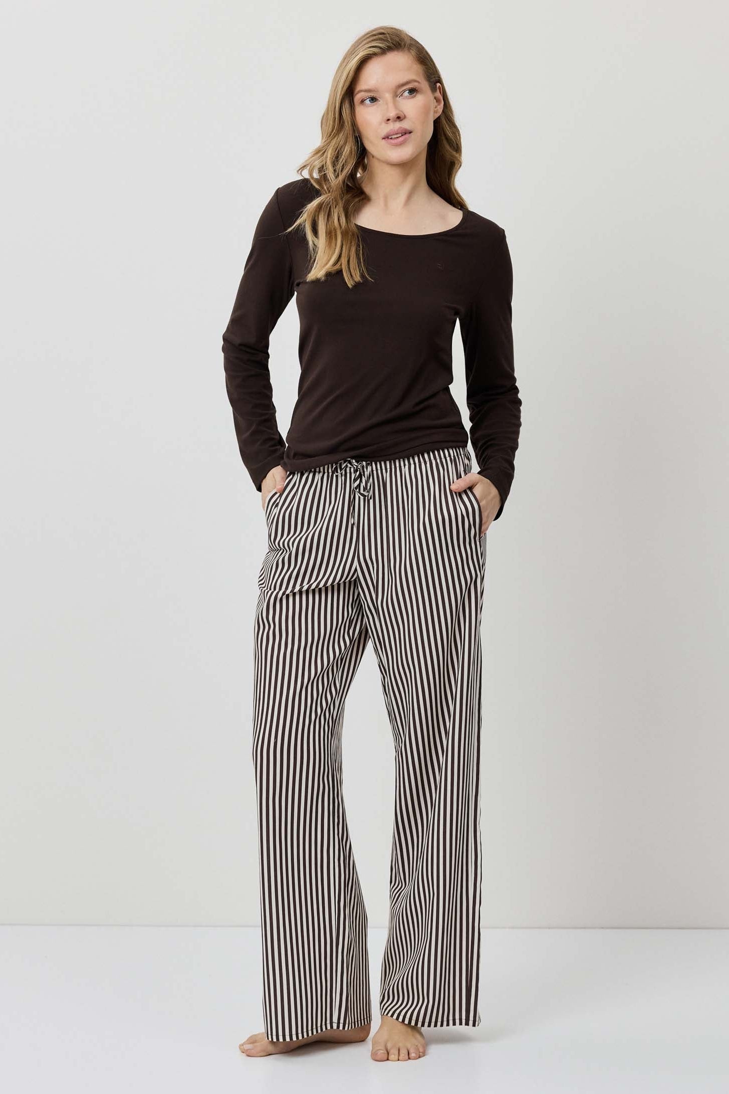 Woman wearing a black long-sleeve top and striped pants on a white background