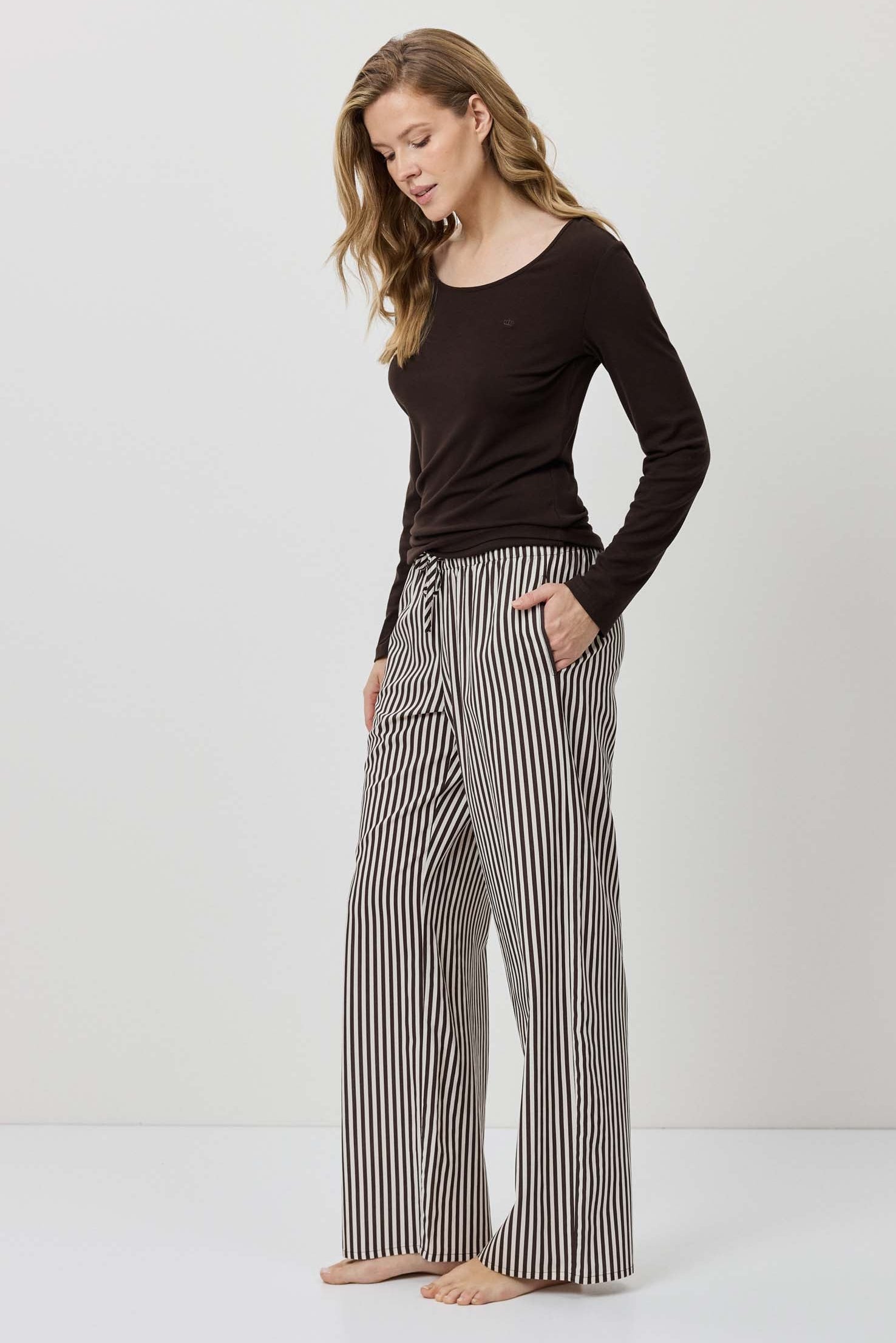 Woman wearing a black long-sleeve top and striped pants on a white background