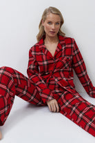 Woman wearing a red plaid pajama set sitting on a white background