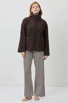 Person wearing a brown jacket and striped pants on a white background