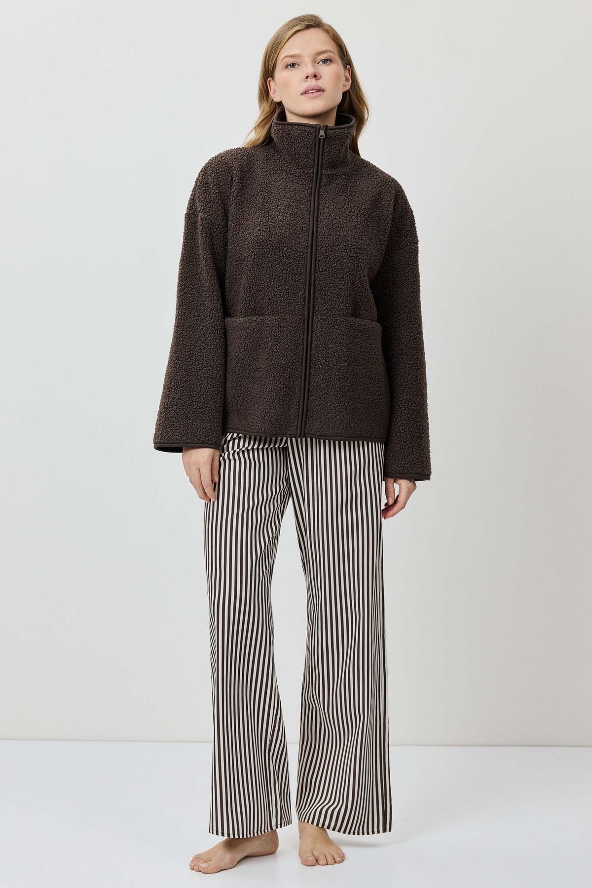 Person wearing a brown jacket and striped pants on a white background