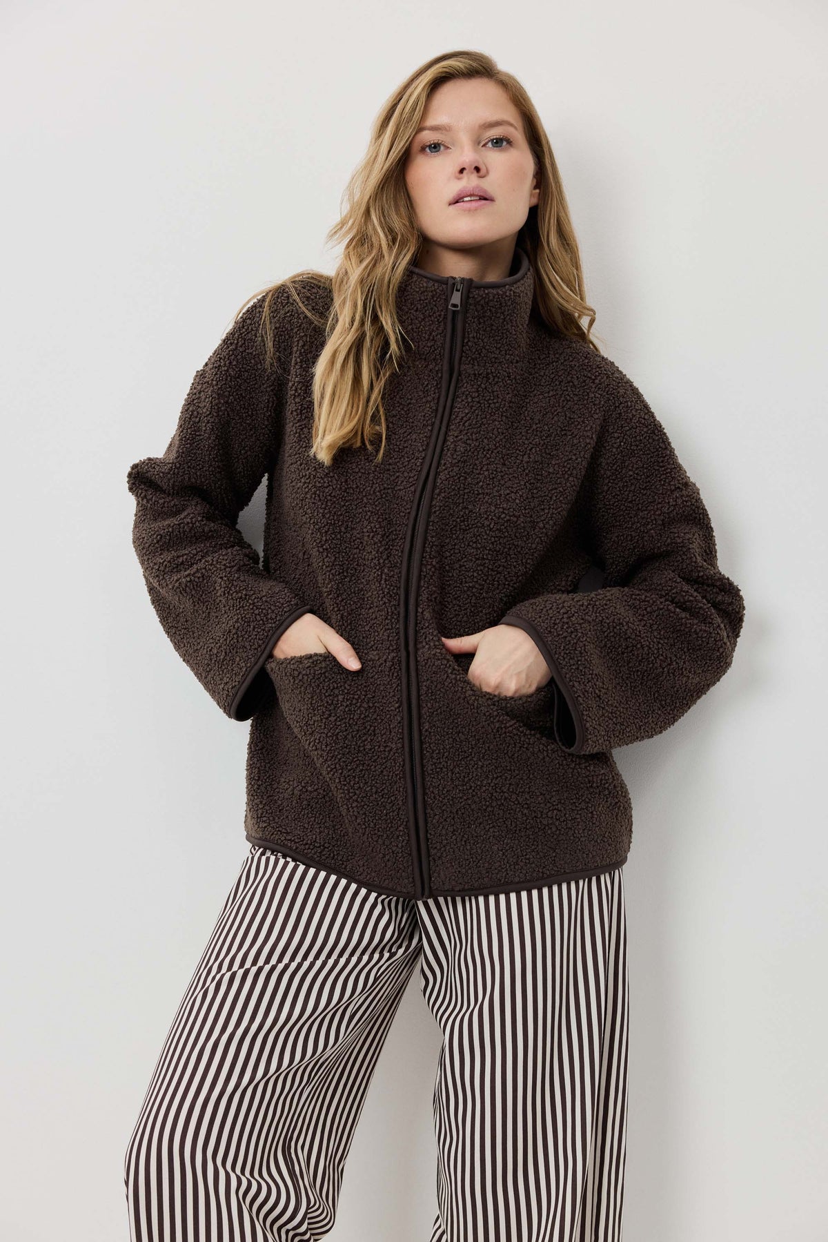 Woman wearing a brown jacket and striped pants against a white background