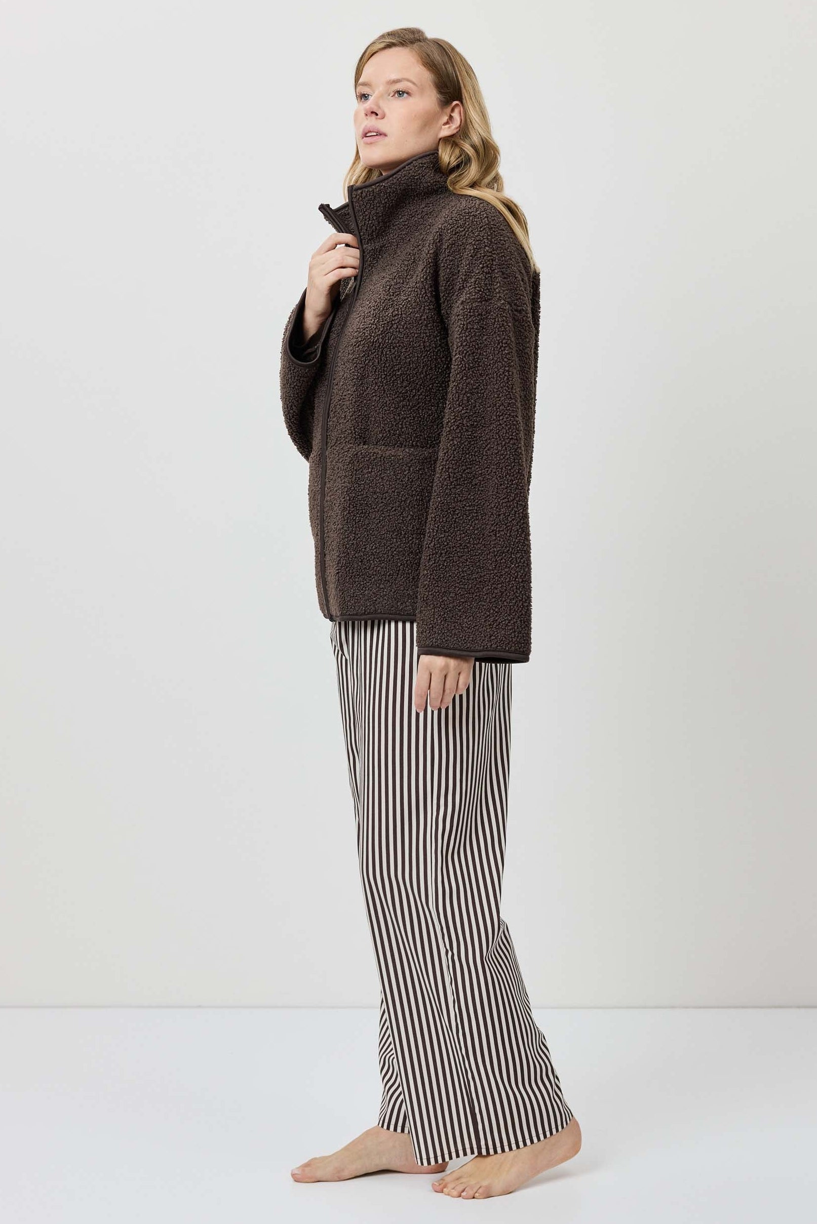 Woman wearing a brown turtleneck sweater and striped pants on a white background