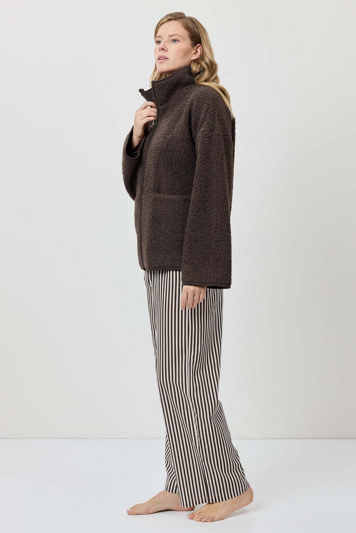 Woman wearing a brown turtleneck sweater and striped pants on a white background