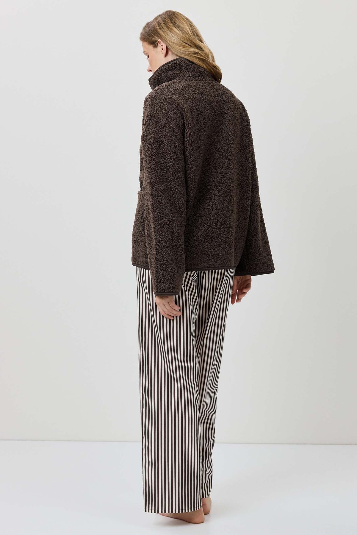 Person wearing a brown sweater and striped pants on a white background