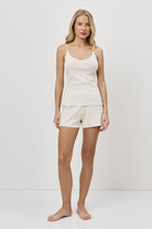 Woman wearing a white tank top and shorts on a plain background