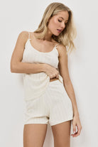 Woman wearing a white sleeveless top and shorts against a plain background