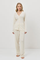 Woman wearing a cream-colored pajama set with pants against a white background