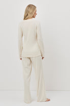 Woman wearing a white pajama set with pants standing against a white background