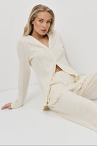 Woman wearing a white pajama set with pants sitting on a white background