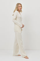 Woman wearing a cream-colored pajam set with pants against a white background