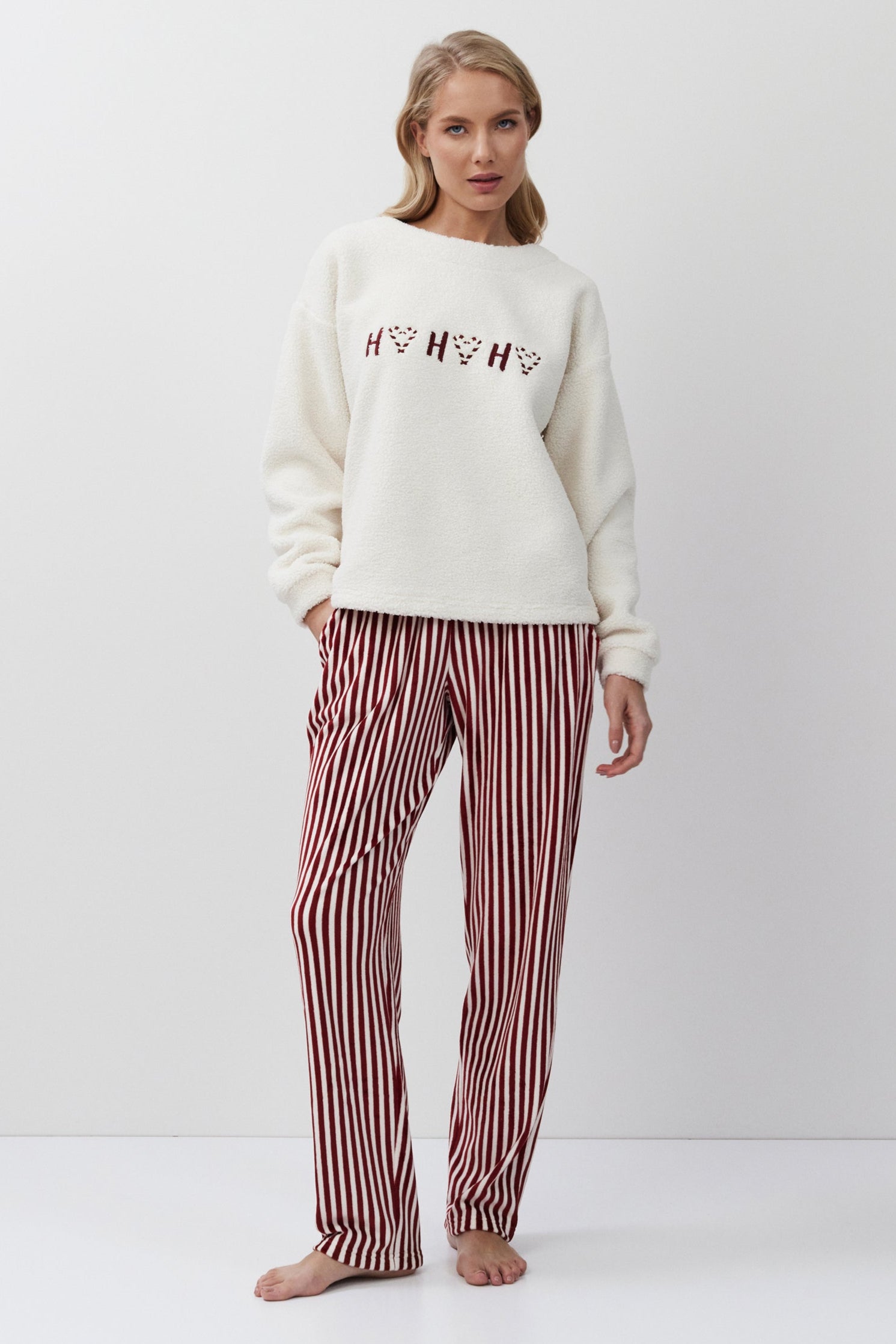 Woman wearing a white sweatshirt with text and red striped pants on a white background