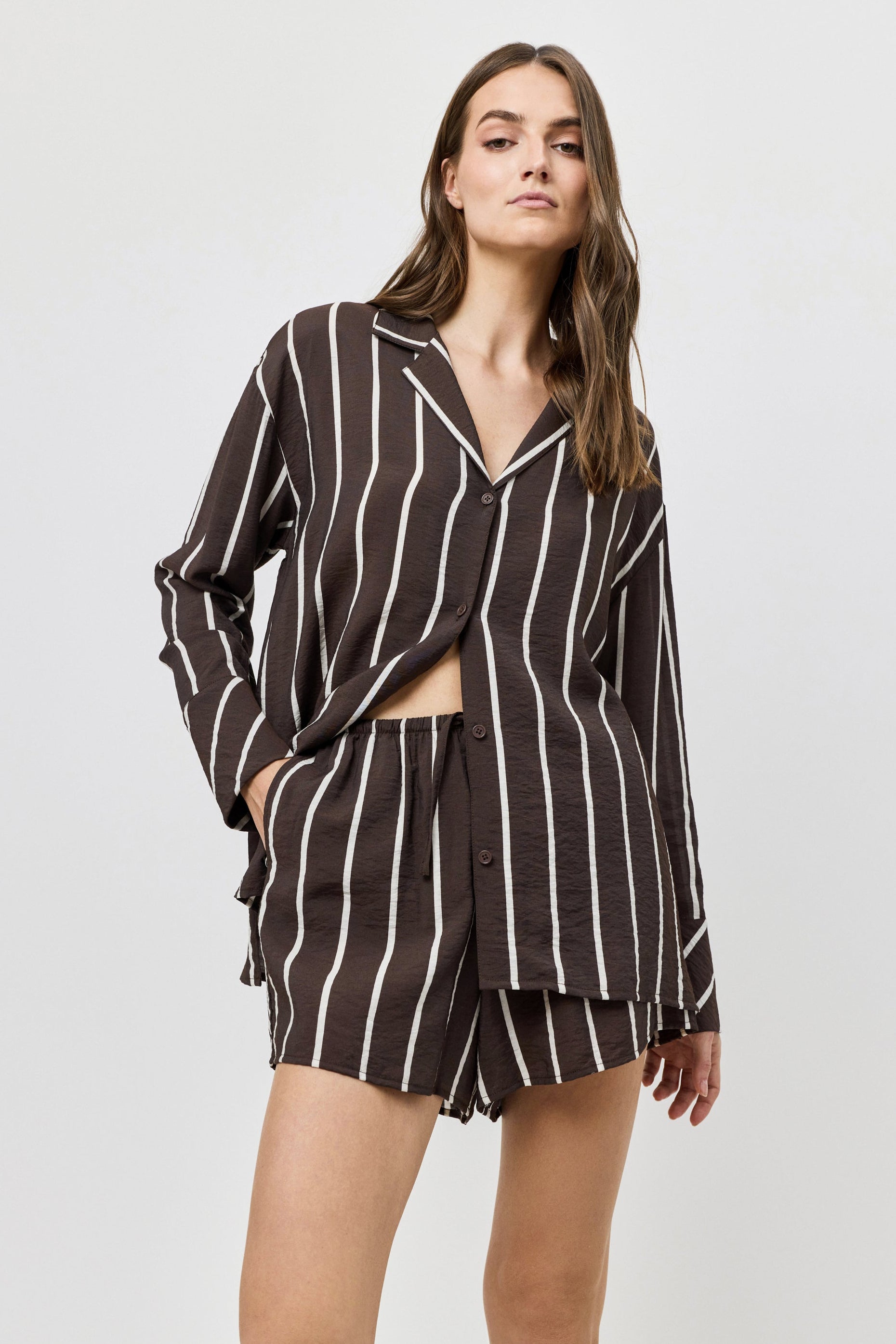 Woman wearing a brown and white striped shirt and shorts on a light gray background