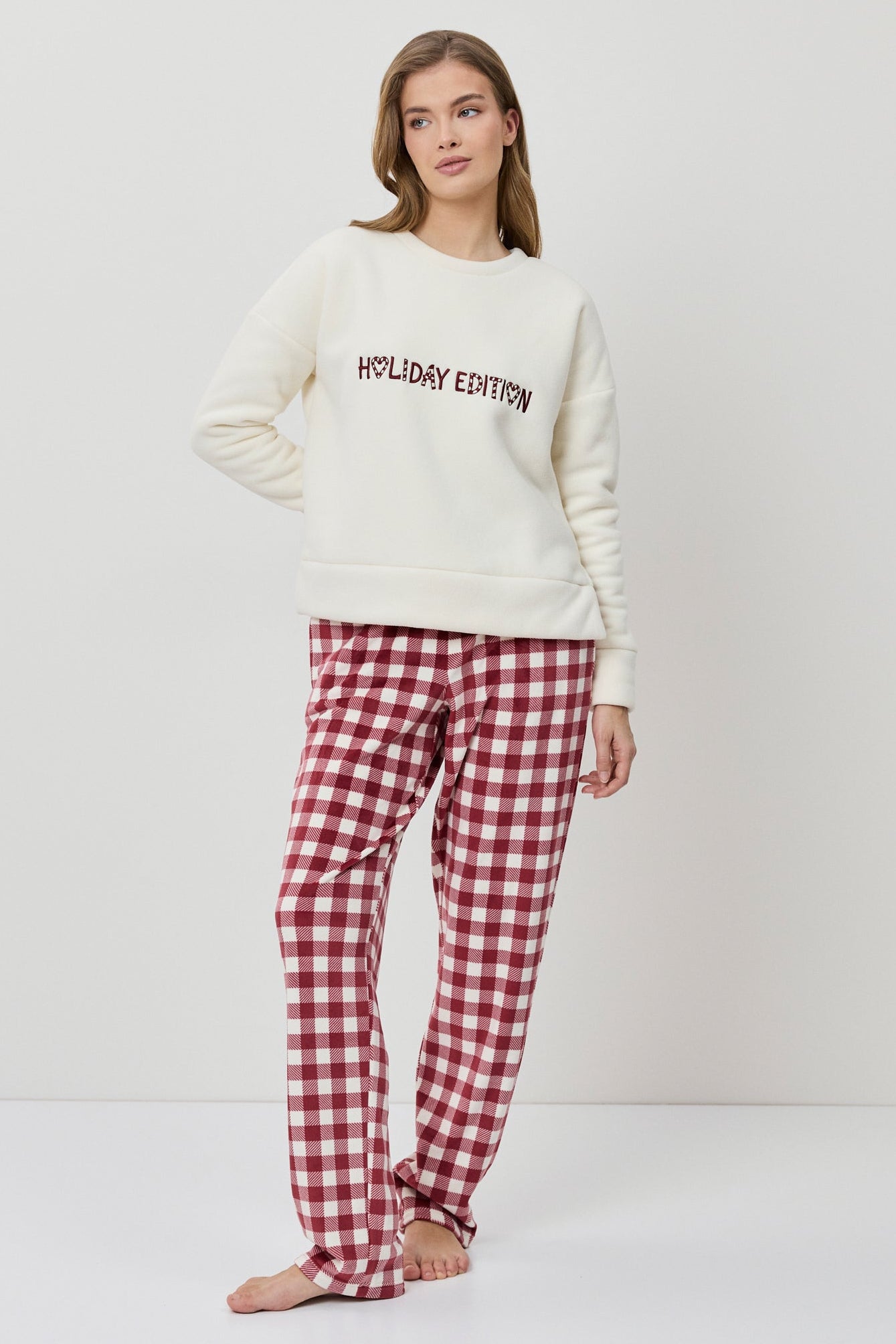 Woman wearing a white sweater with text and red plaid pants on a white background