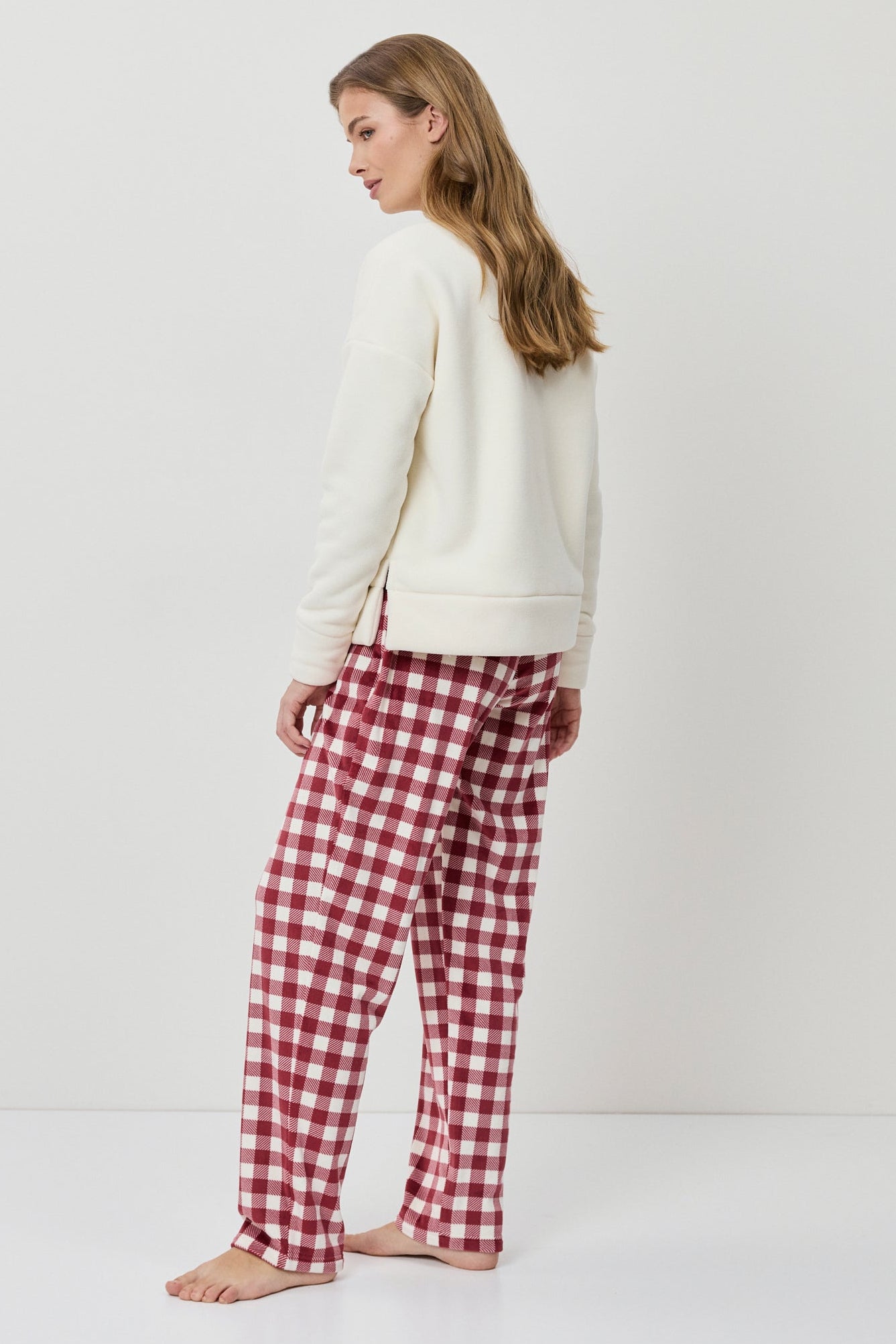 Woman wearing a white sweater and red plaid pants on a white background