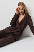 Woman wearing a brown resort wear set sitting on a white floor against a white wall.